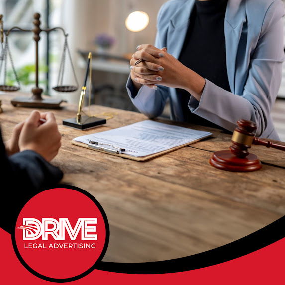 An attorney sitting at a wooden desk with hands clasped during a legal consultation with a client, featuring a gavel, scale of justice, and Drive Legal Advertising LLC branding.