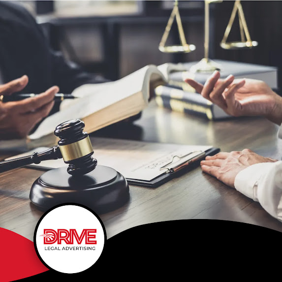 Attorneys discussing case strategy around an open law book with a gavel and scales of justice on the desk, branded for Drive Legal Advertising LLC.